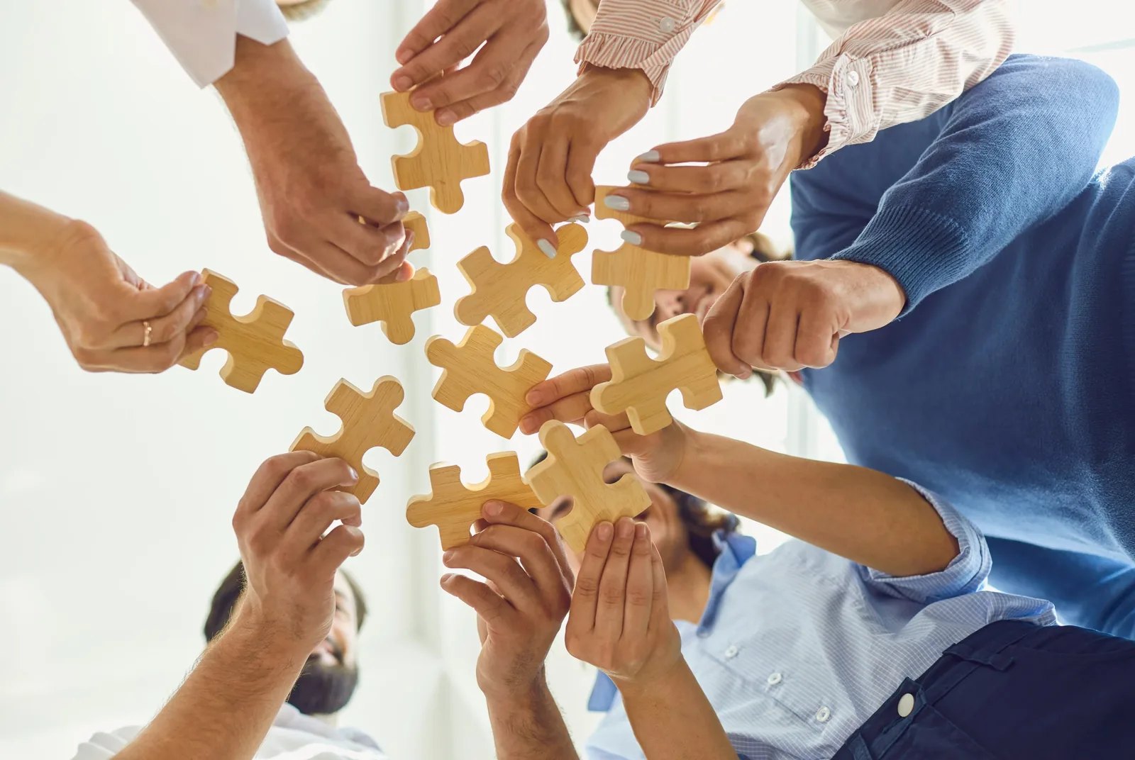 Several pairs of hands bringing puzzle pieces together, representing collaborative and individually shaped support